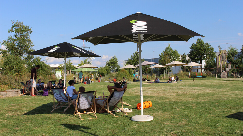 Menschen in Liegest&uuml;hlen unter Sonnenschirmen.