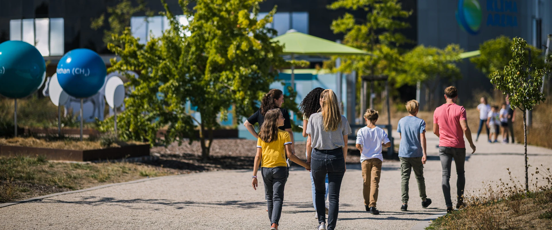 Famile l&auml;uft durch die Au&szlig;enanlage auf das Geb&auml;ude der KLIMA ARENA zu.
