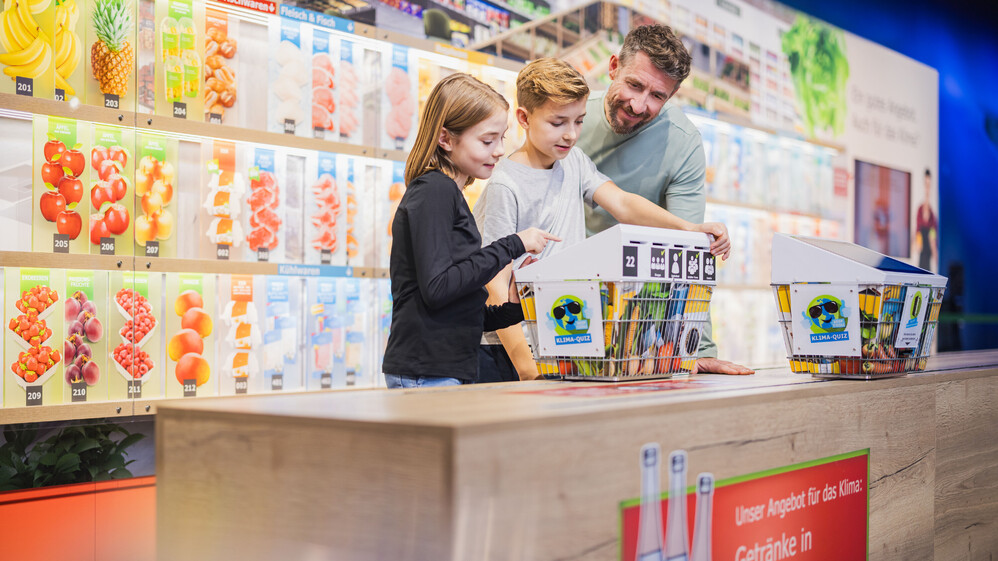 Ein Vater mit zwei Kindern bei Bedienung des interaktibven Einkaufsterminal im Klima-Supermarkt.
