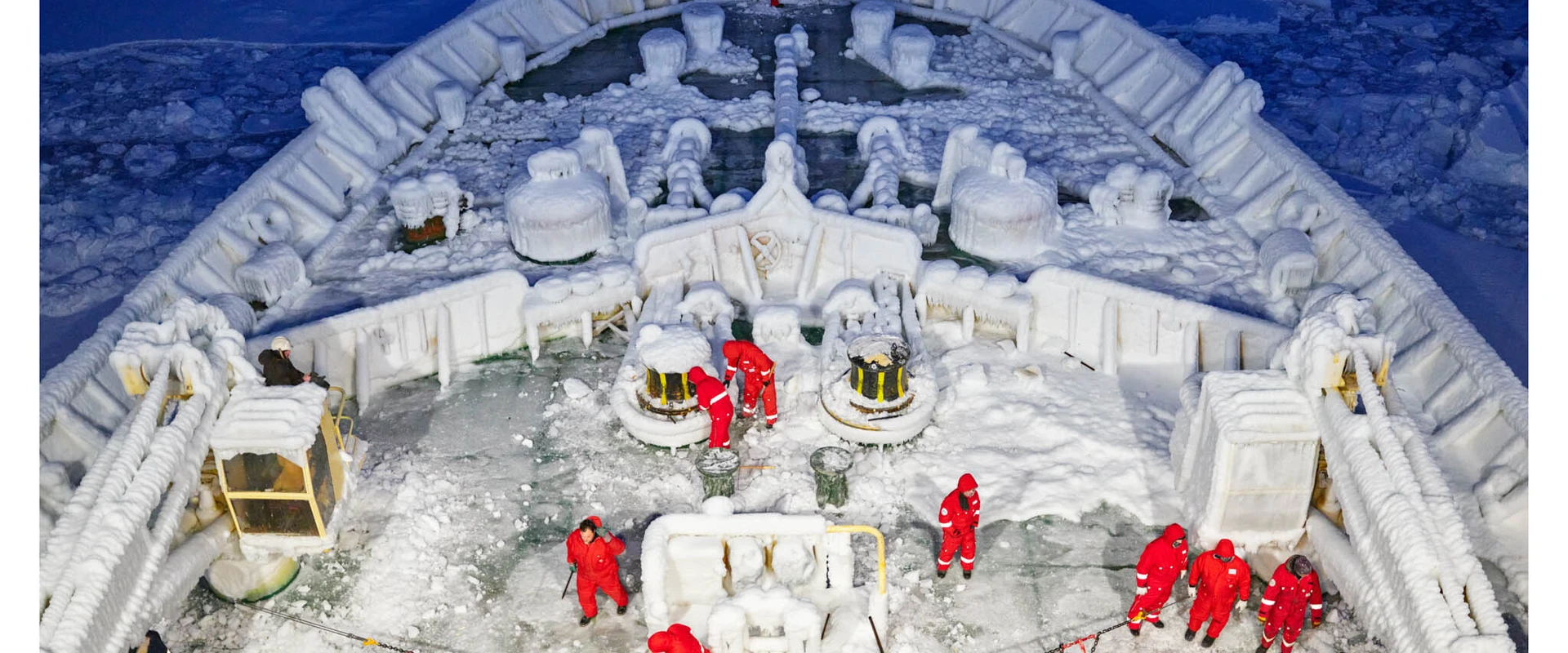 Der Vorderteil eines mit Eisschicht &uuml;berzogenen Schiffes, auf dem Wissenschaftler in Schutzanz&uuml;gen arbeiten.