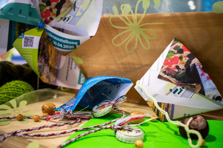 Auf dem Bild sind gebastelte Fangbecher aus Papier sowie Schn&uuml;re und kleine Naturmaterialien auf einem Tisch zu sehen.
